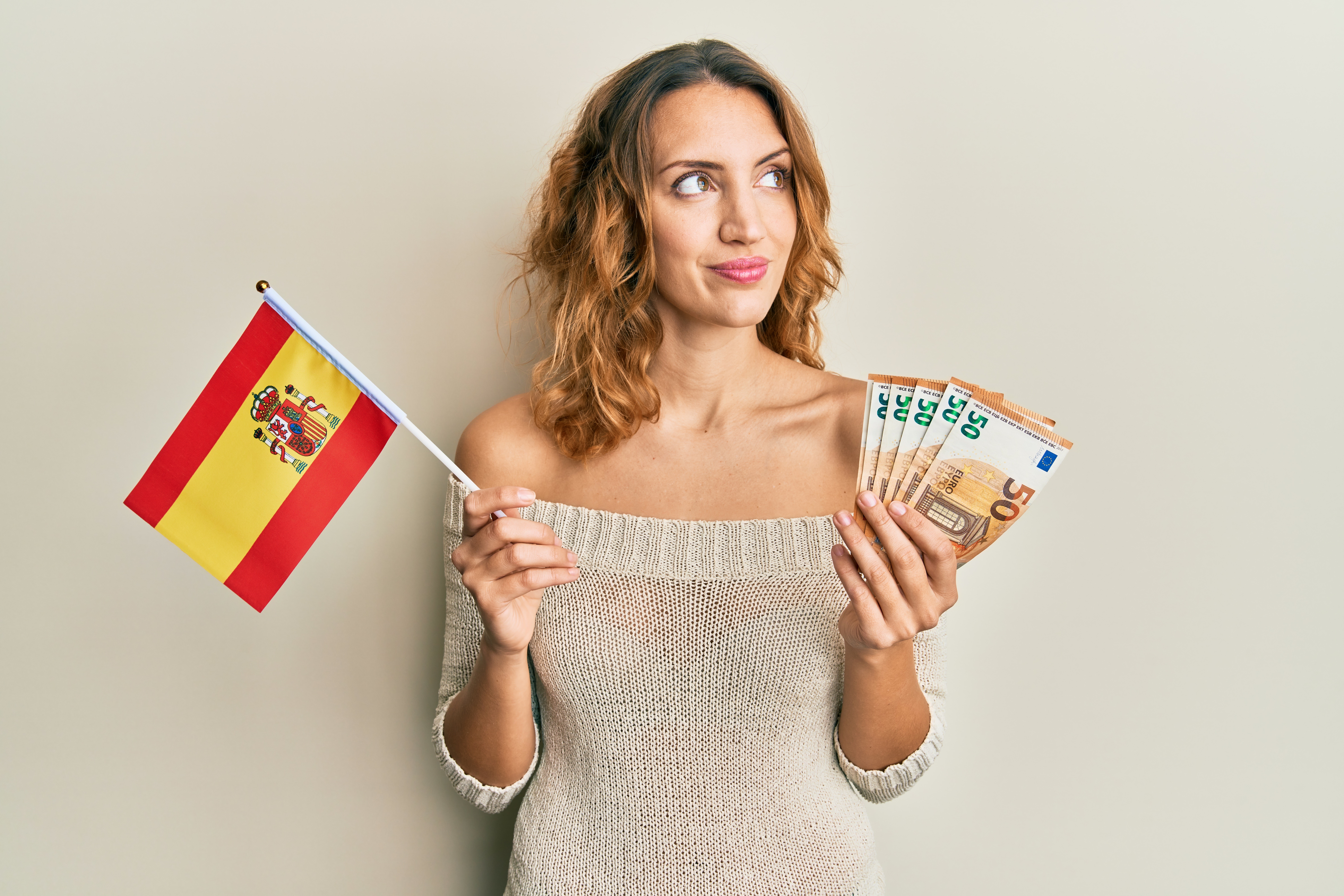 Una mujer sonriente sosteniendo una bandera de España y un abanico de billetes de euro, simbolizando la recepción de dinero desde el extranjero en España.
