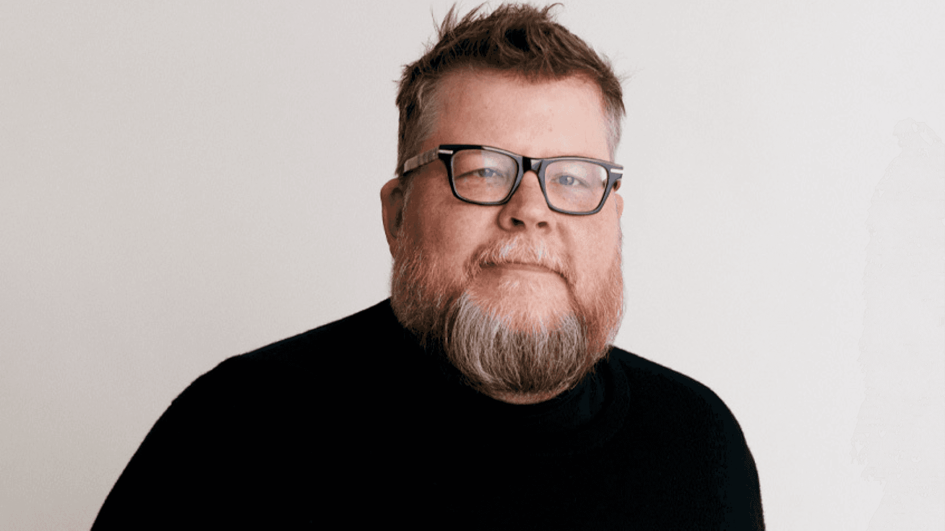 Etsys Chief Product and Technology Officer Rafe Colburn, ein bärtiger Mann mit Brille in schwarzem Shirt, lächelt leicht vor weißem Hintergrund.
