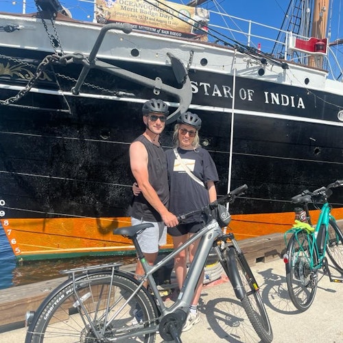 两位戴着头盔的人在阳光明媚的日子里，站在停靠在港口的“印度之星”船前，身旁是自行车。
