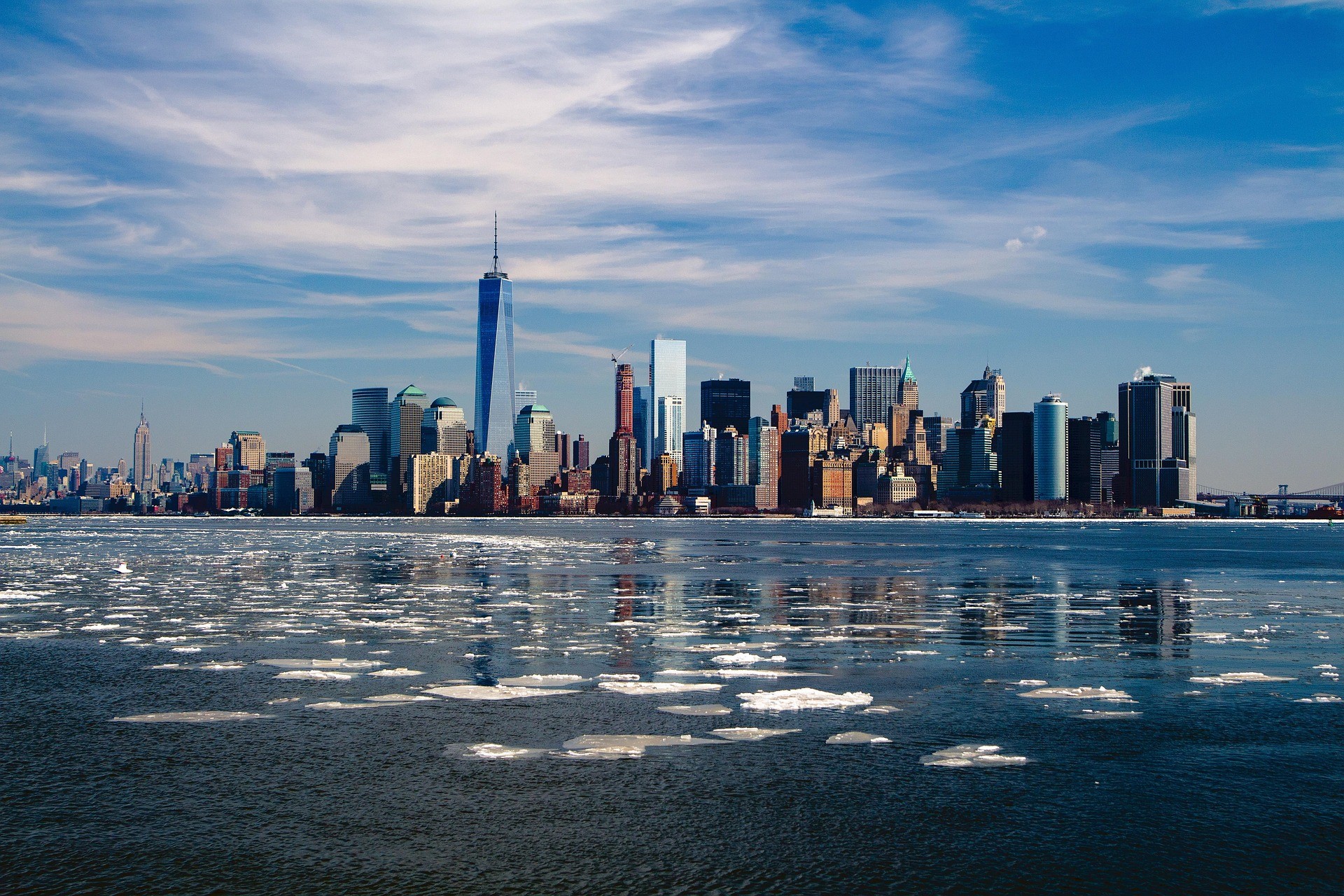 New York City skyline and One World Trade Center across a river with floating ice.