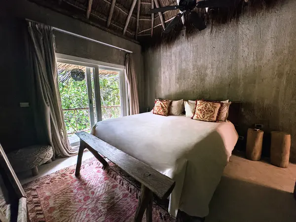 Standard Room at Nômade Tulum, with bed, pillows, and jungle view through large windows.
