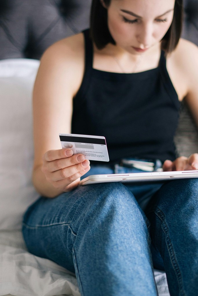 closeup of a newcomer to Canada's hands holding multiple Canadian debit and credit cards over a payment terminal; representing successfully opening a bank account based on the required identification checklist.