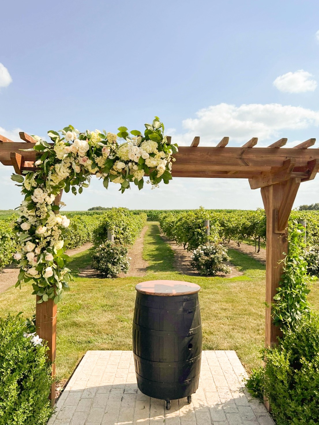 Wedding ceremony arch with white floral arrangements at vineyard venue designed by Des Moines Iowa florist