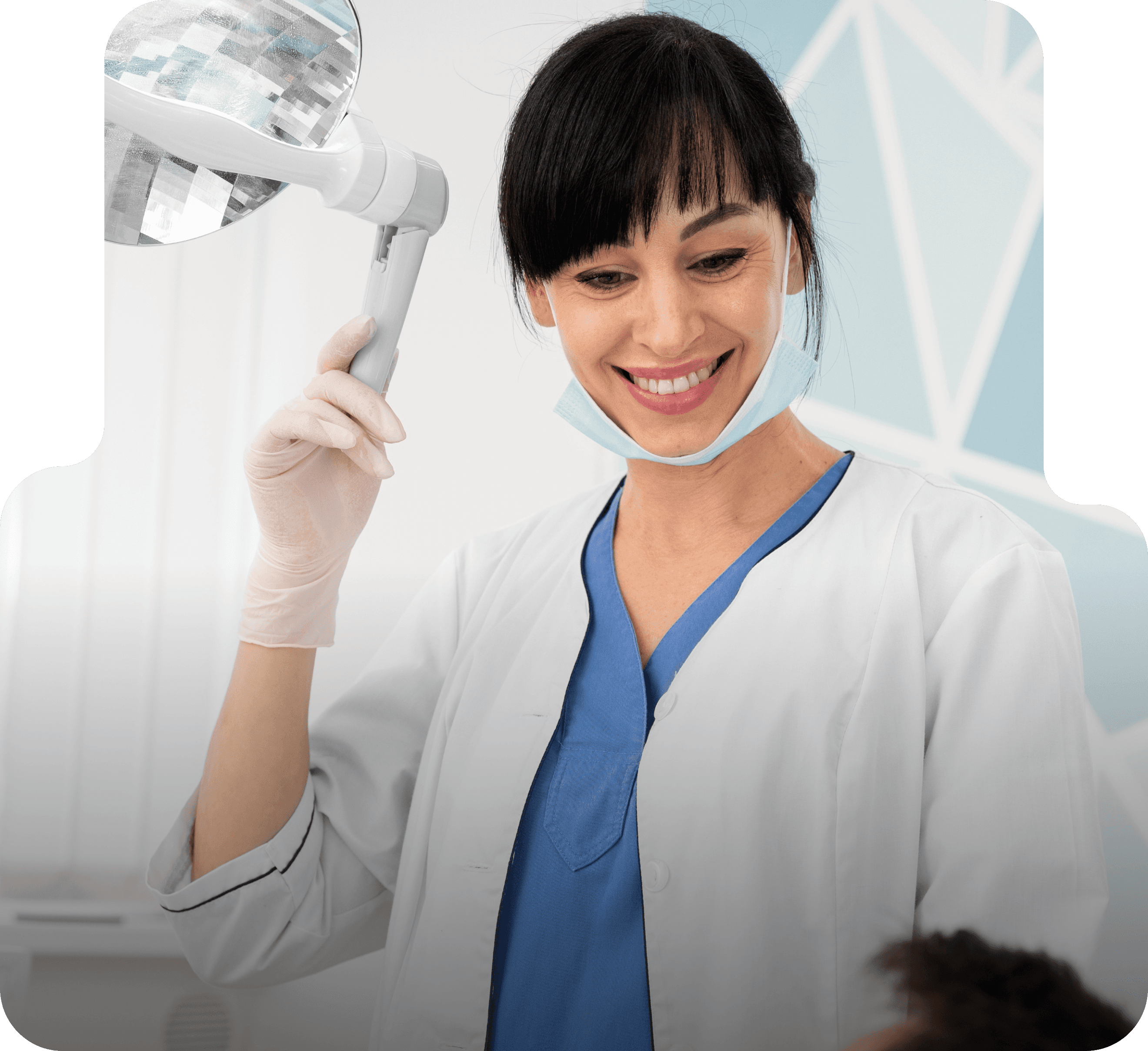 A smiling dental professional wearing a mask and gloves, adjusting an overhead dental light