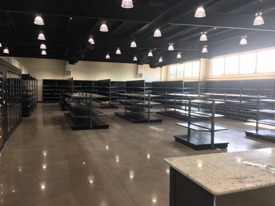 A spacious, empty room with multiple glass cooler cases, empty retail shelving and bright overhead lights.