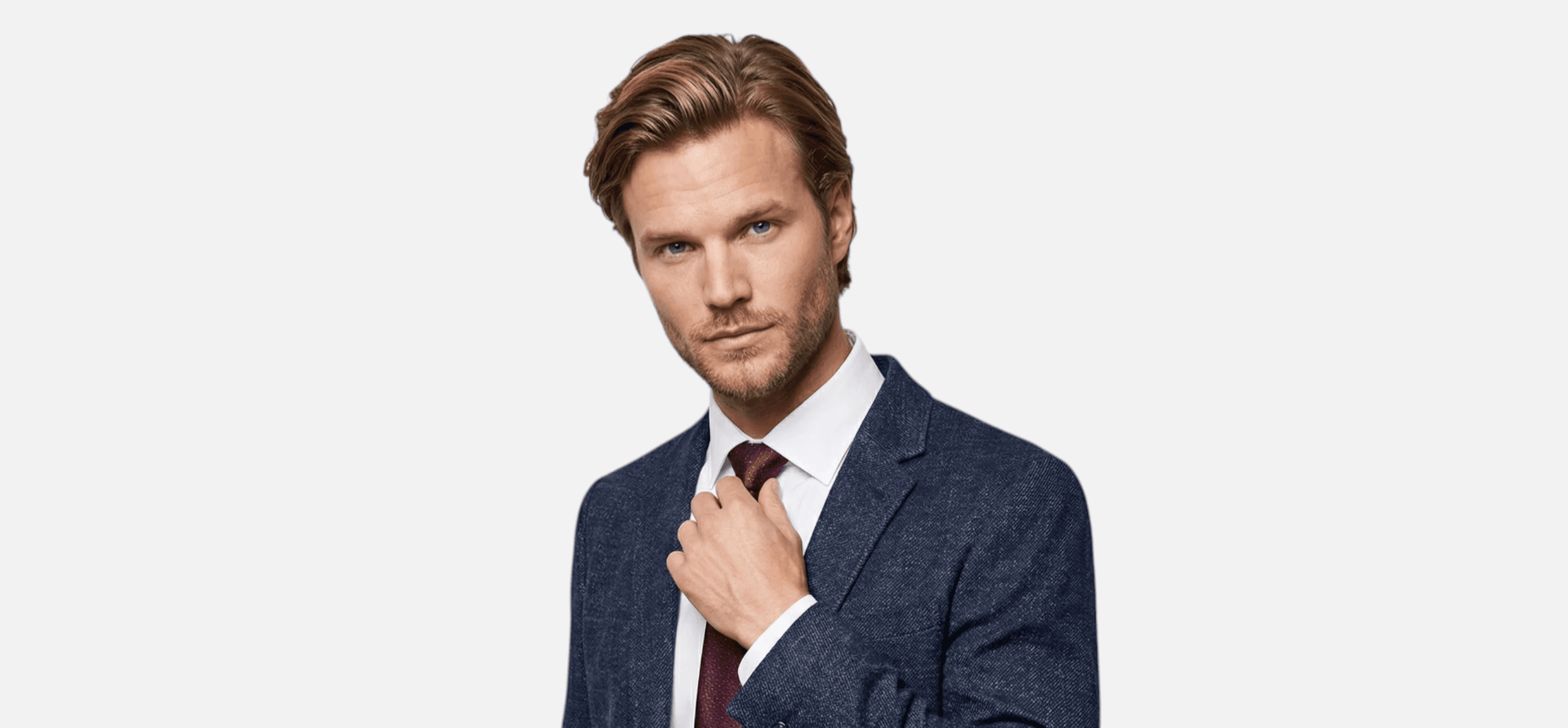 A man in a suit adjusts his tie, looking confidently at the camera against a plain background.
