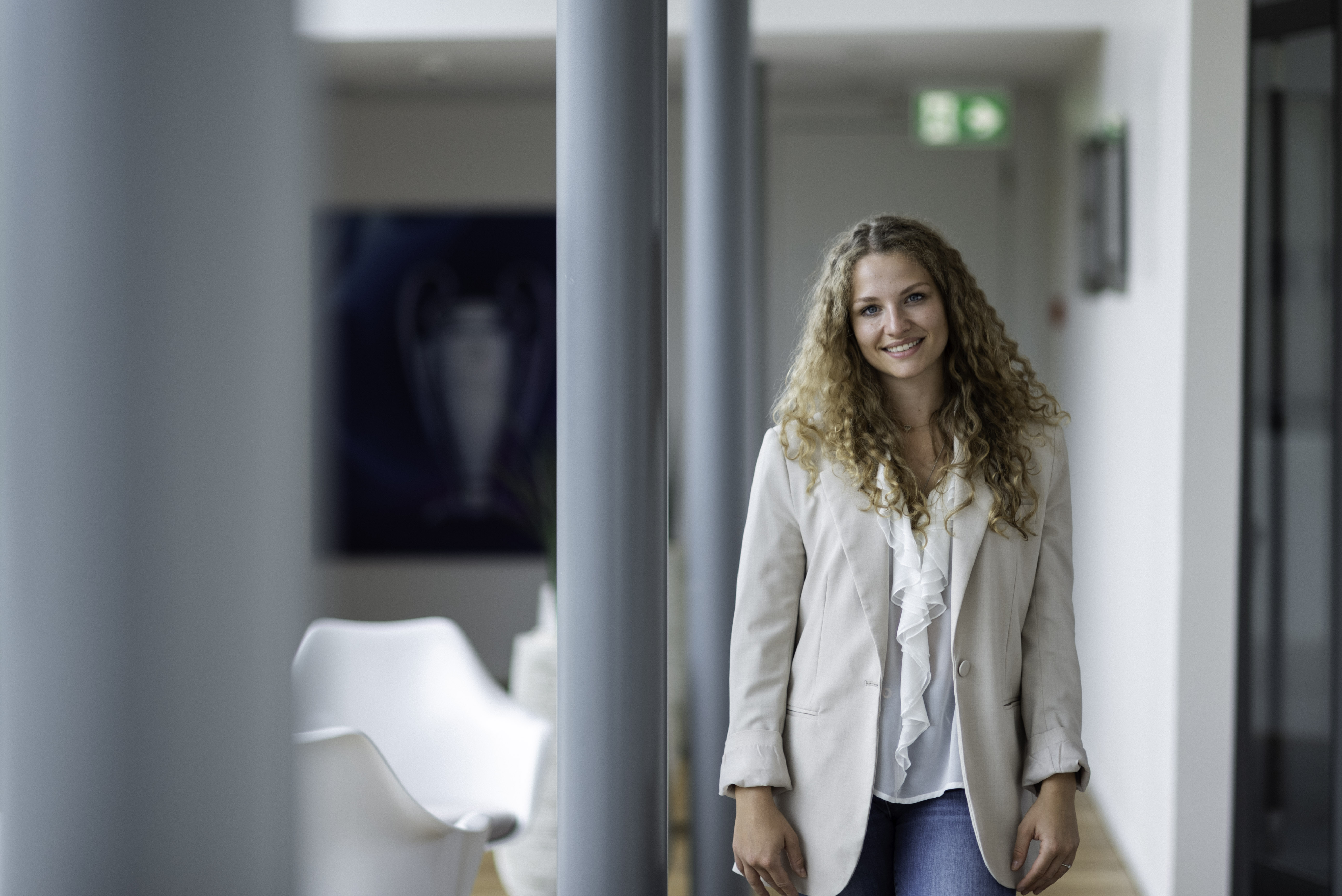 Lächelnde Frau aus dem Team steht selbstbewusst in einem Flur und vermittelt eine warme und professionelle Präsenz.