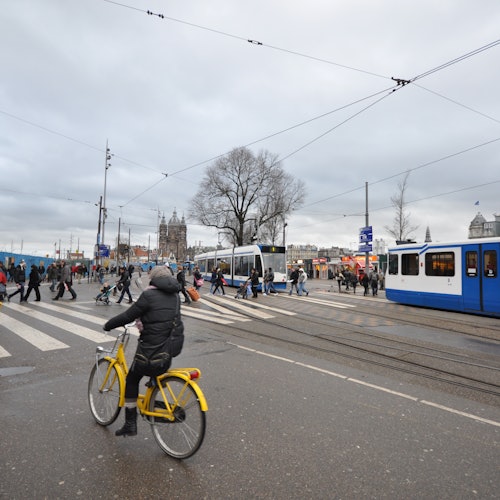 一个骑着黄色自行车的人穿过繁忙的街道，与行人、电车和头顶的电线交错在一起，天空阴云密布。