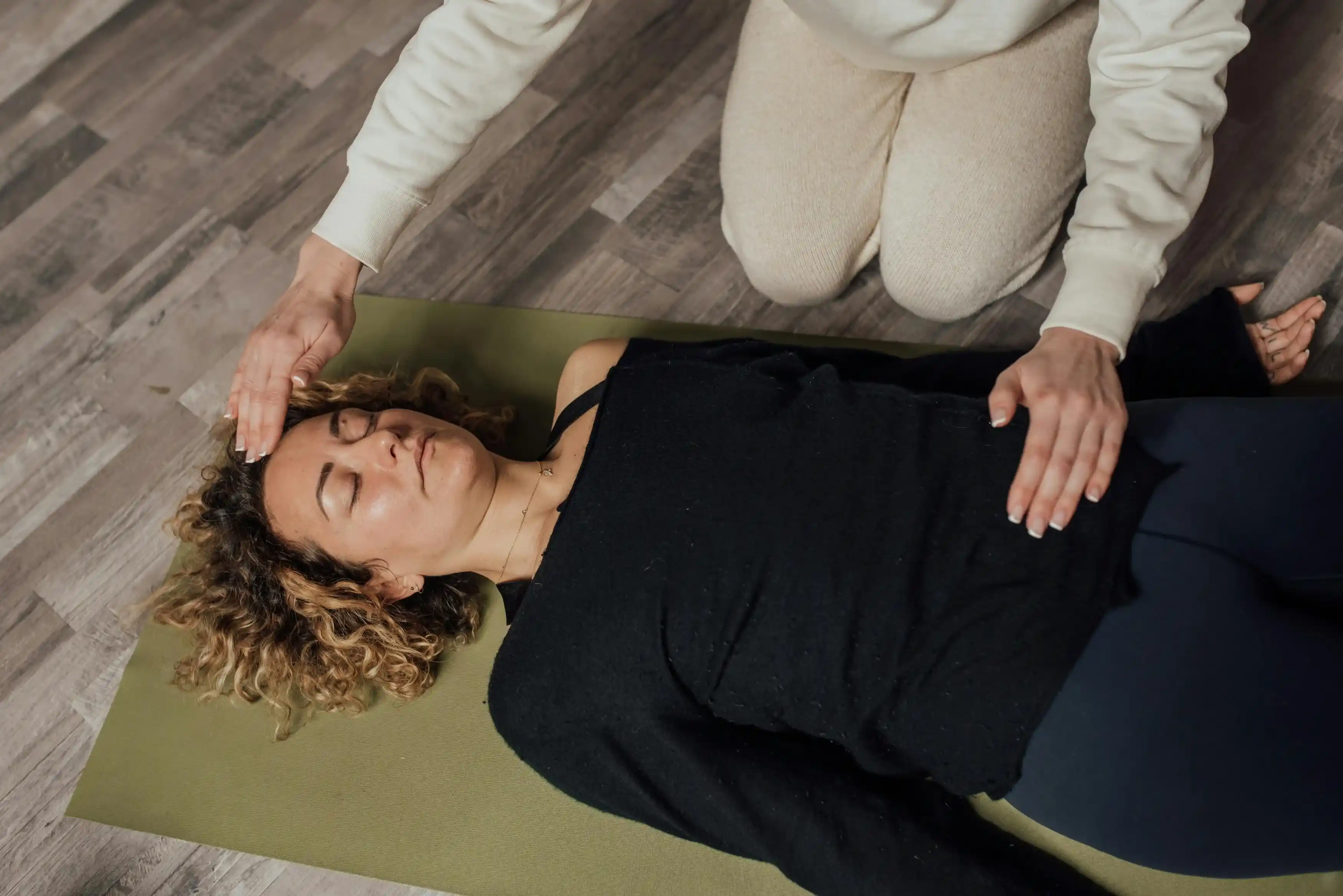 Hand rolls green yoga mat on light surface near plants.