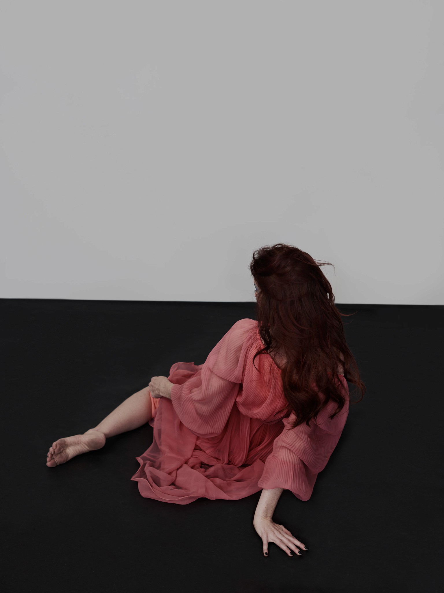 A modern photographic editorial portrait of a woman laying on the floor turned away from the camera. She is wearing a pink dress and is in an expressive pose. 