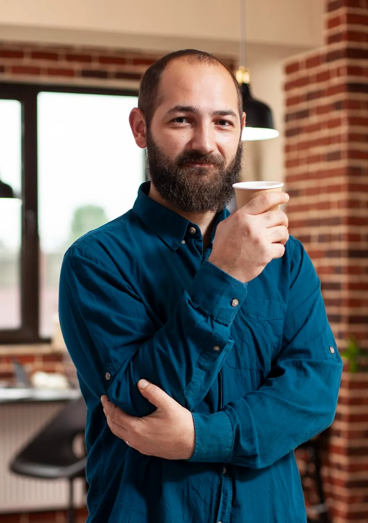 Marcus Tan, Project Manager, holding a coffee cup in a professional workspace with brick background.