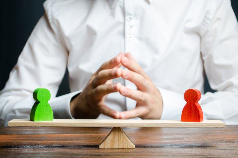 A man with hands in the lock and looks at the rival red and green figures on a scales. The concept of conflict resolution and the search for a compromise in the dispute. Weighted decision