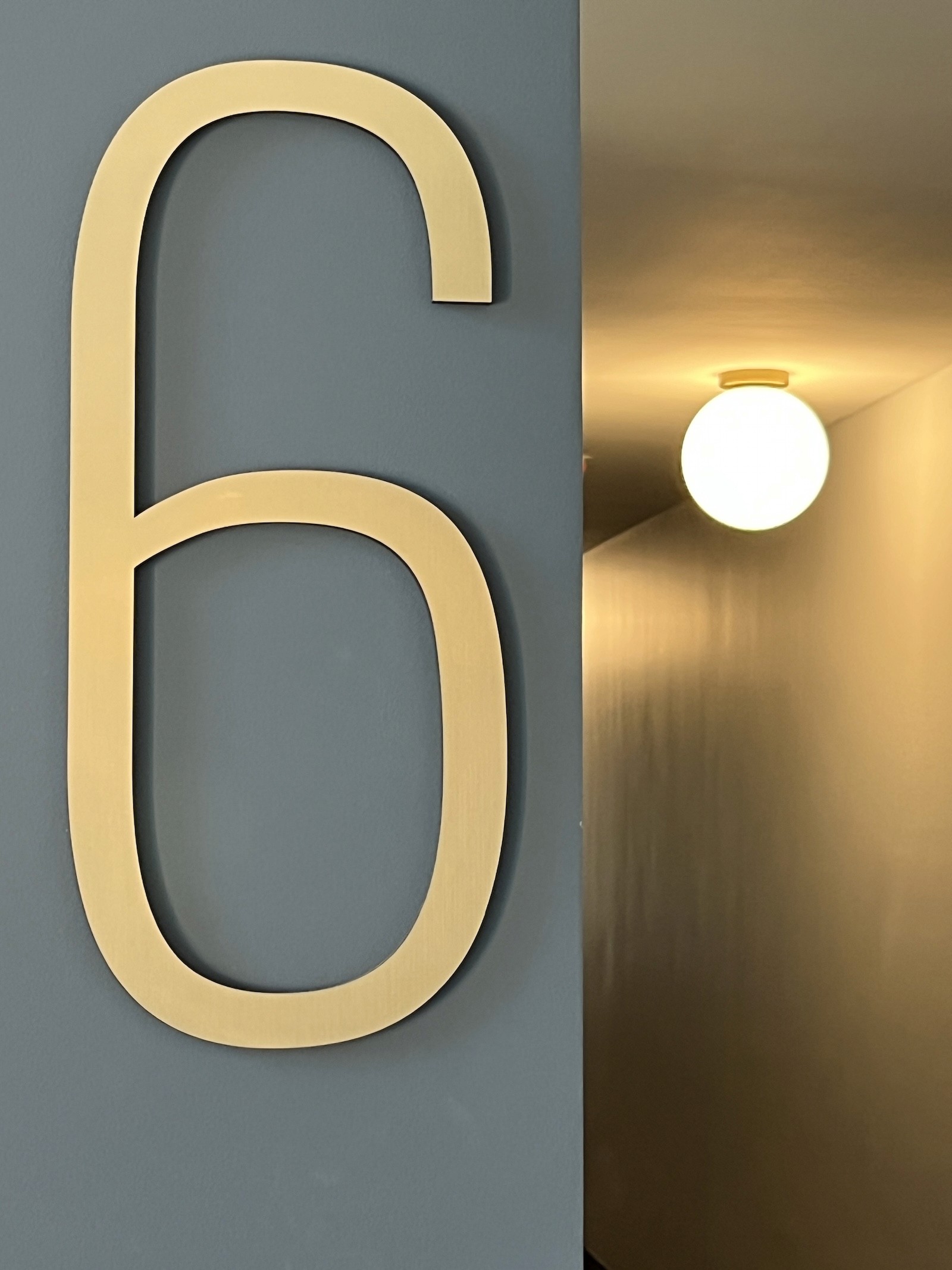 A large gold number "6" on a light gray wall next to a warm, glowing wall light.