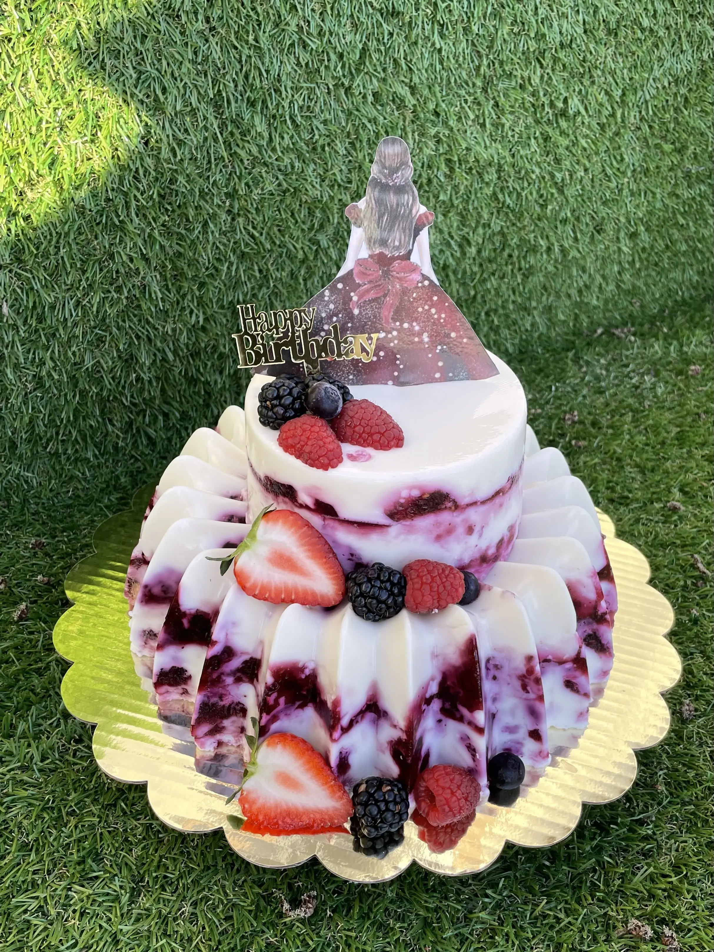 Layered gelatin cake decorated with fresh berries and a cake topper featuring a celebratory figure. A unique design that combines texture and vibrant colors, perfect for special occasions. Susa’s Sweets & Balloons.