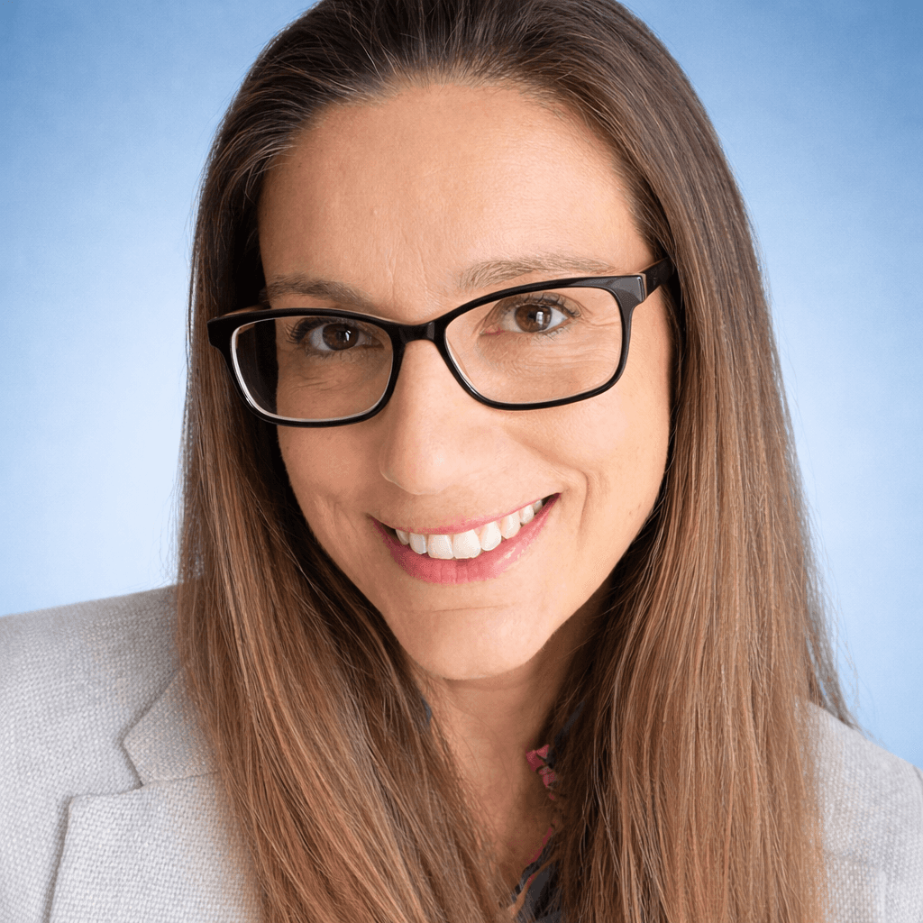 A person stands outdoors in a natural setting with lush green trees under a clear sky, wearing a dark sweatshirt, and looking into the distance.