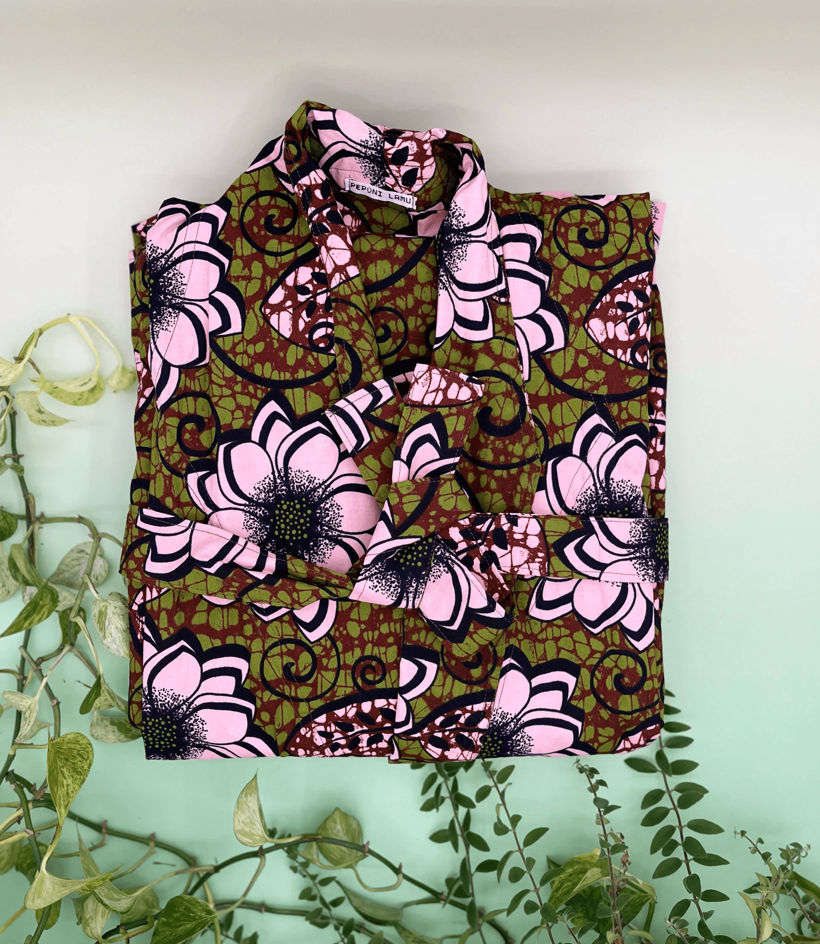 Floral printed robe folded surrounded by pothos vines.