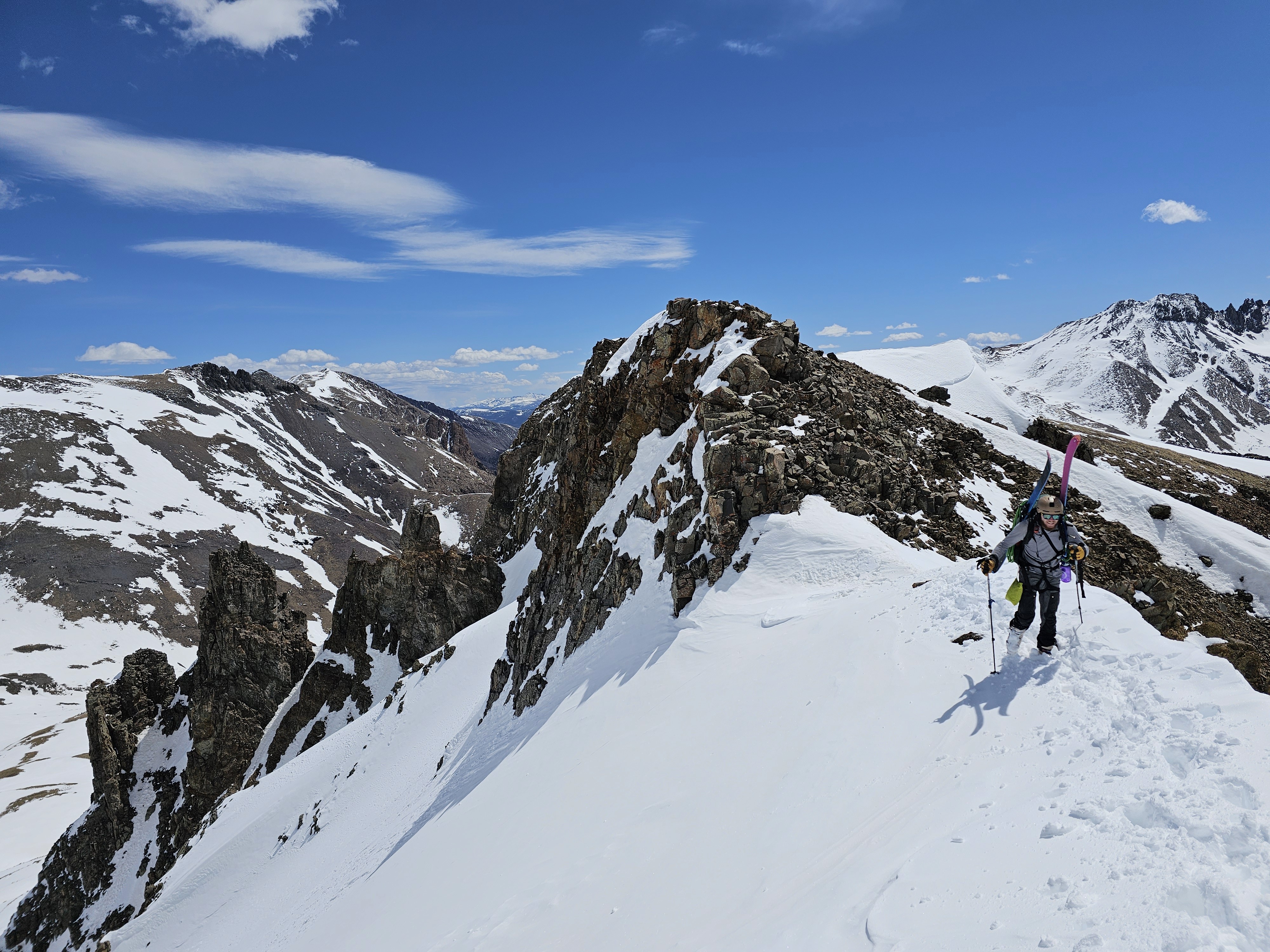 Skier traverses the top of a couloir with snowy peaks in the background