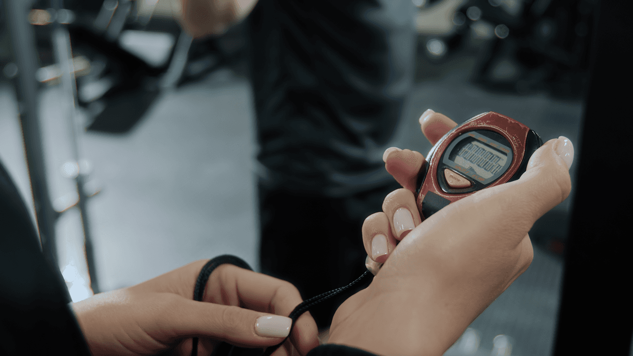 Person holding a handheld stopwatch in a gym while timing an exercise