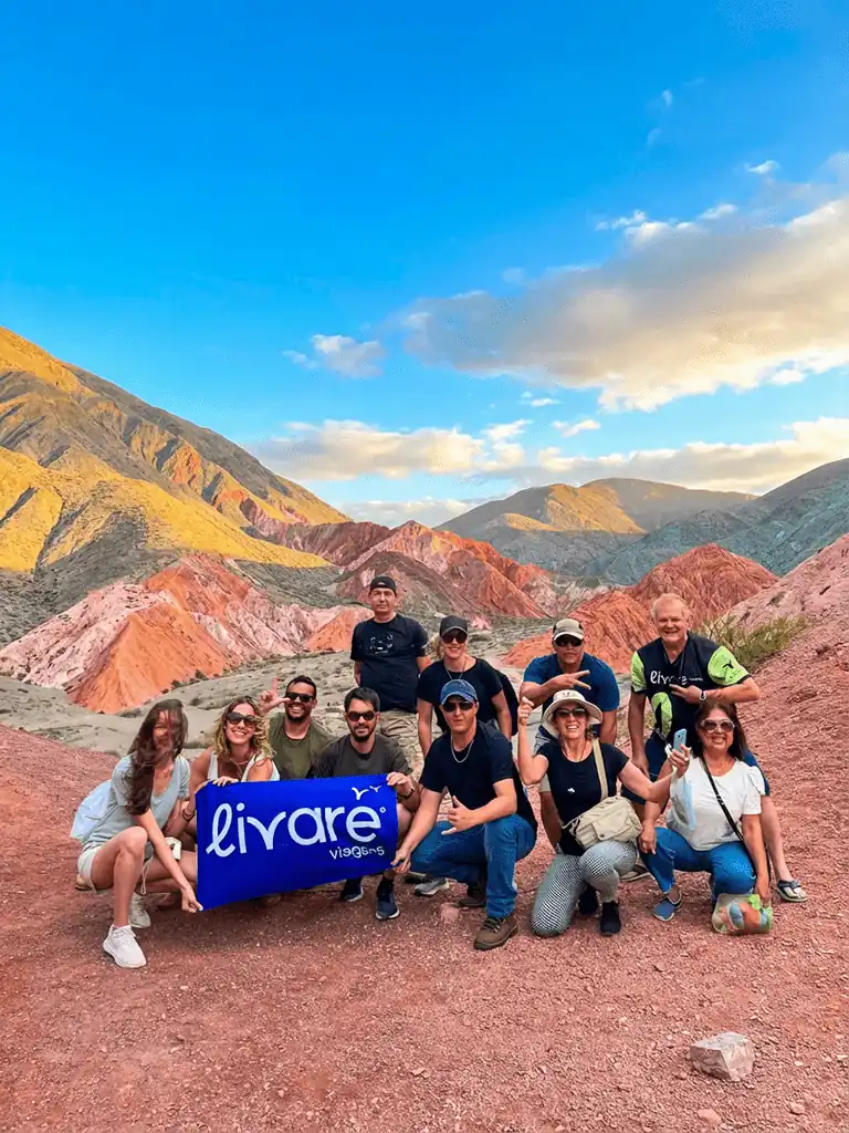 Grupo de viajantes da Livare posando na Montanha das Sete Cores, em Purmamarca, com formações rochosas coloridas ao fundo