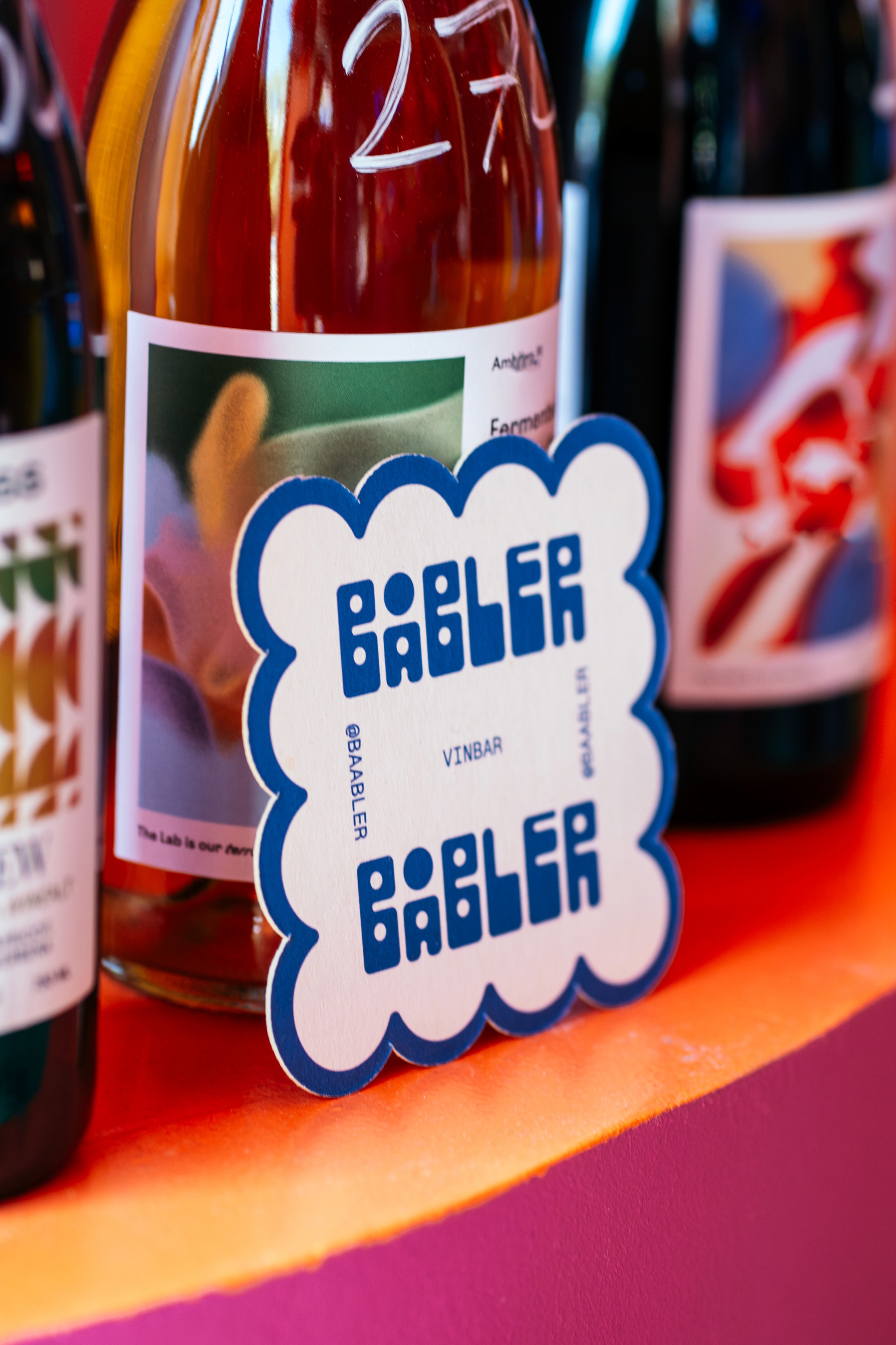 Coaster design for Båbler wine bar leaning on a bottle of wine.