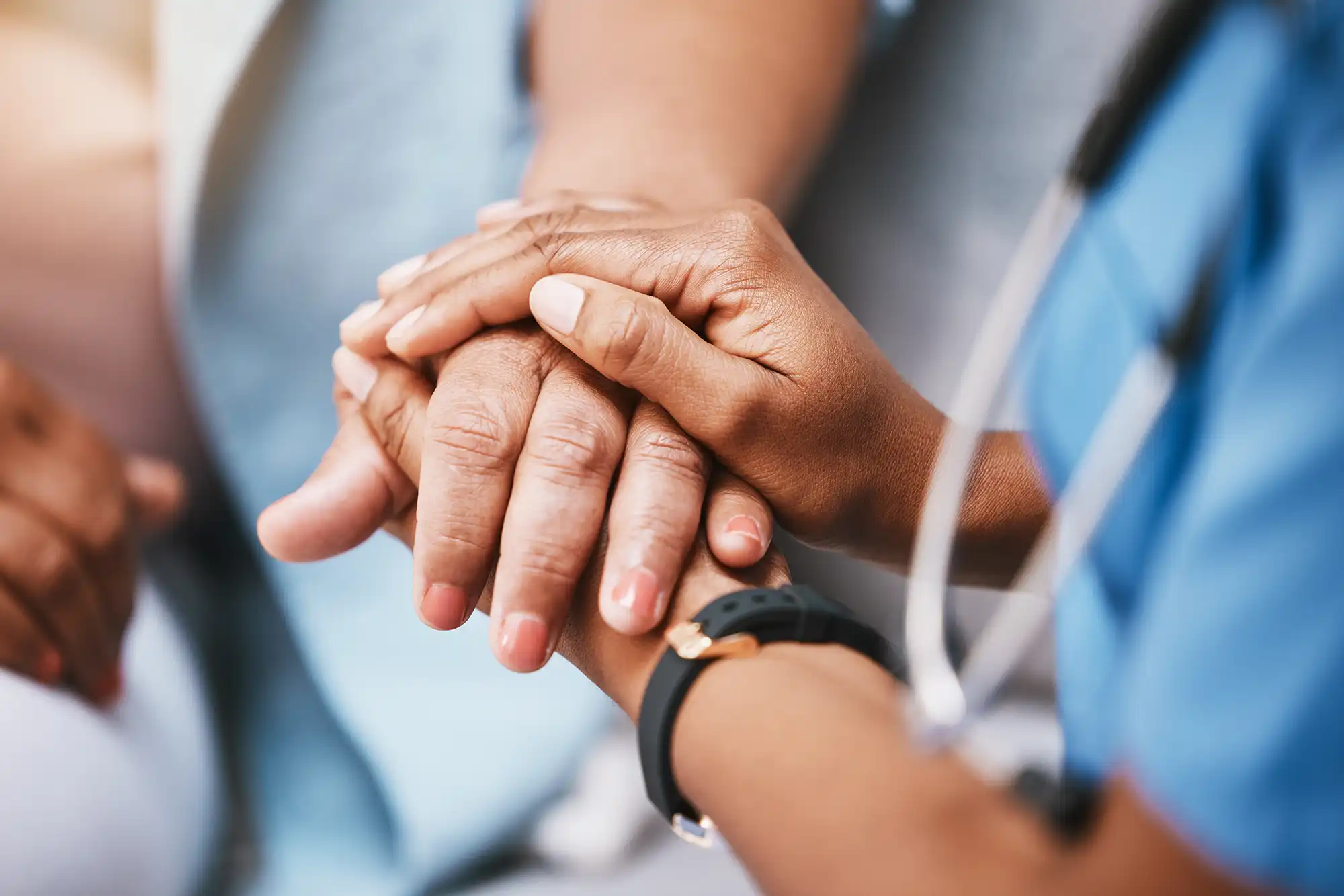 Close-up of a healthcare professional holding a patient's hands for support.