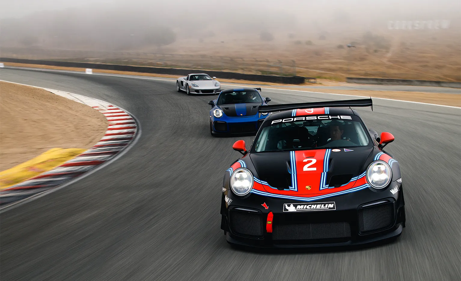 Three Porsche race cars rounding a turn on the track.