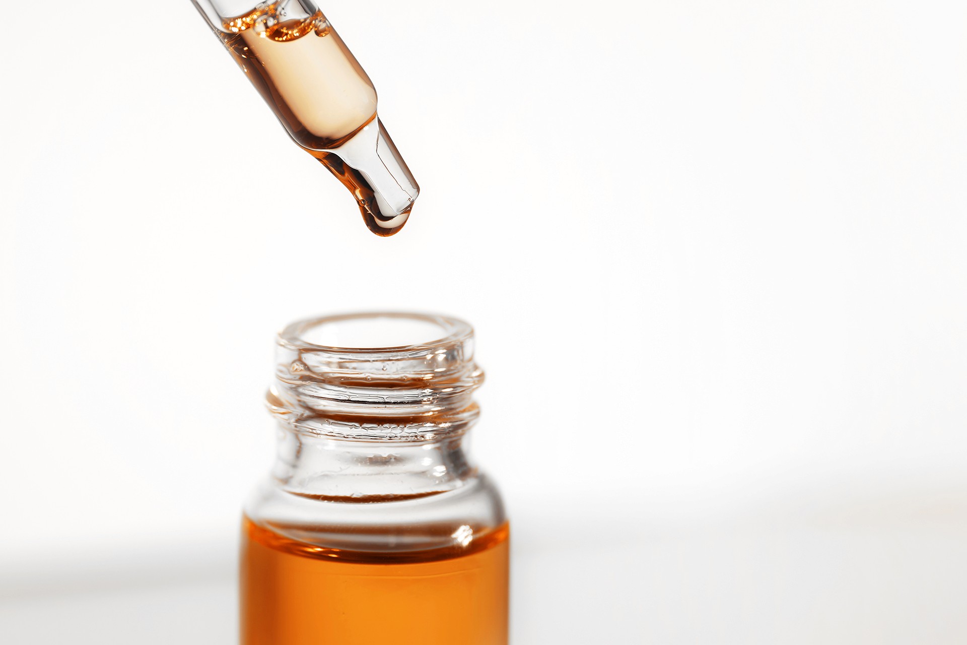 A syringe filled with essential oil is being applied to a glass bottle.