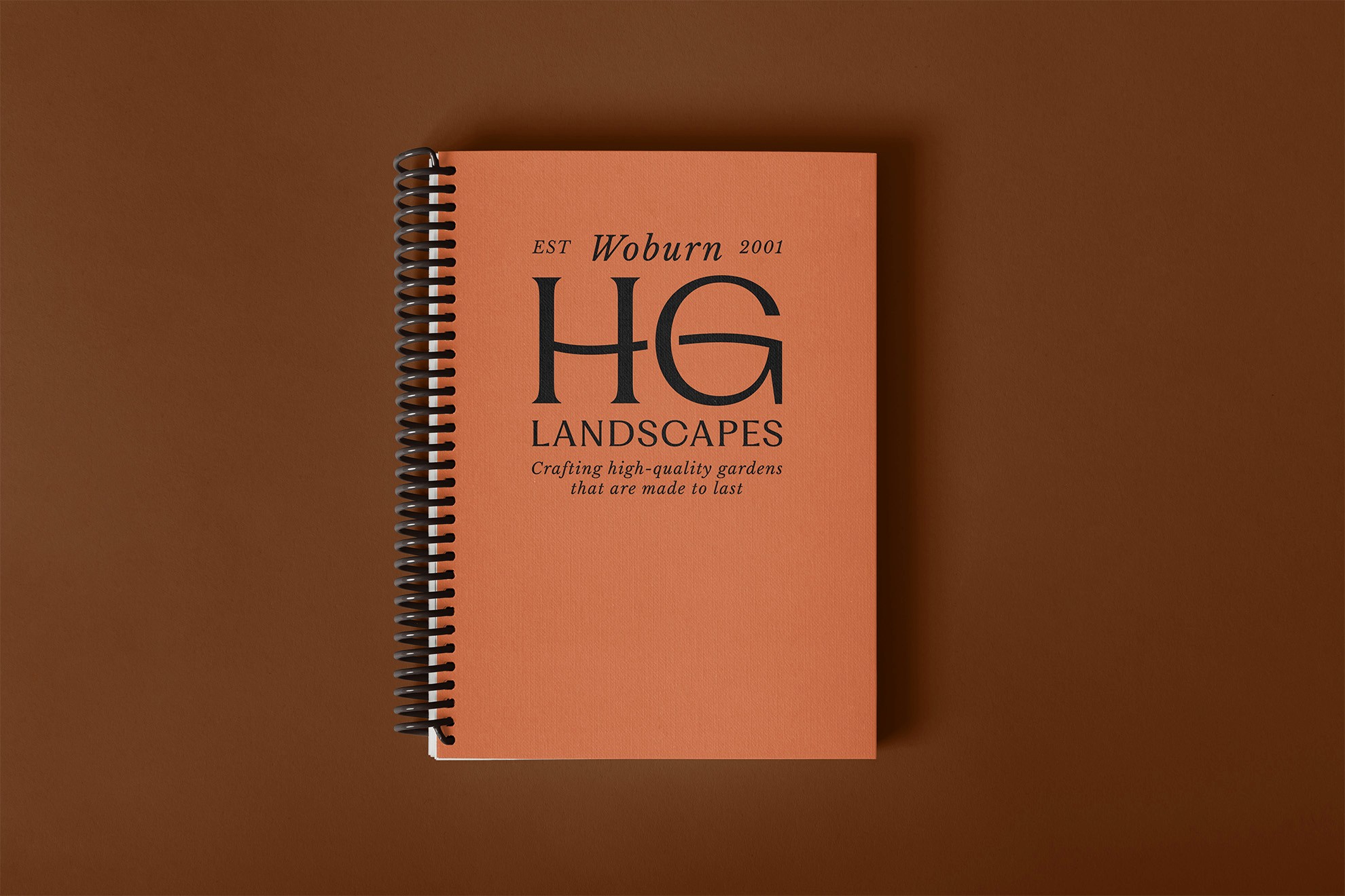 A closed book with an orange cover featuring the letters "HG" embossed in the center, set against a brown background.