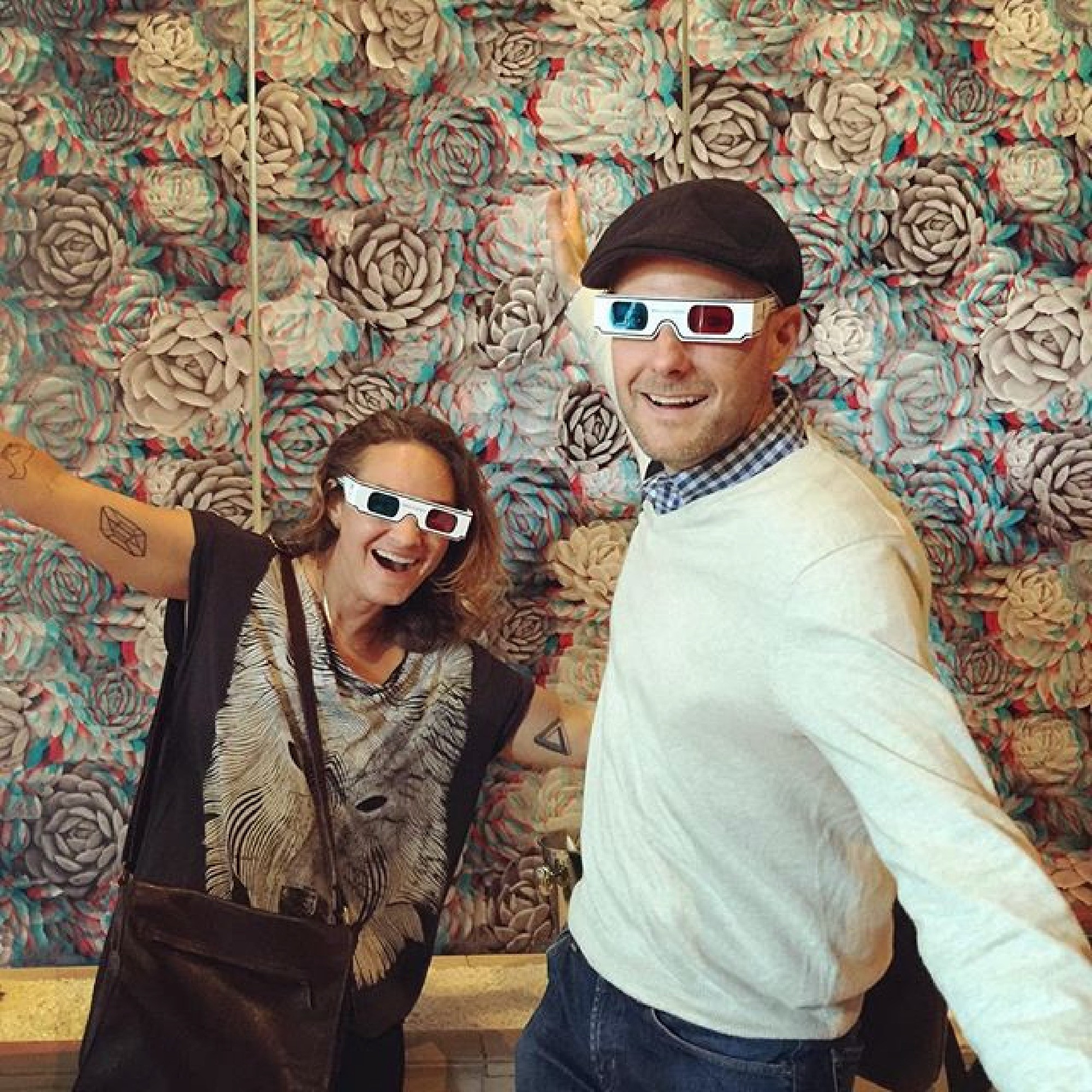 Rob Hartnett and Sarah Strauss wearing 3 D glasses and posing in front of digitally printed 3 D wallpaper of cacti that look like roses.
