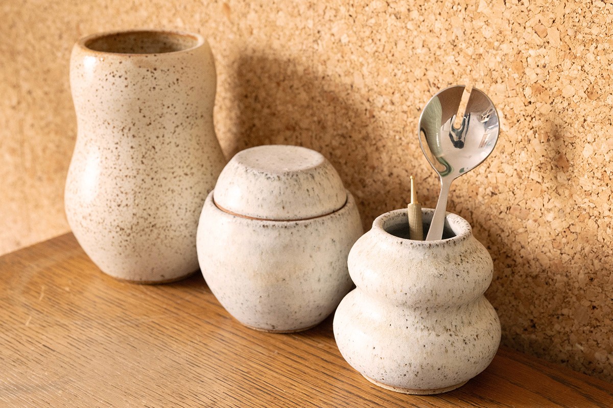 Handmade ceramic jars containing acupuncture supplies on a wooden table against a cork wall.