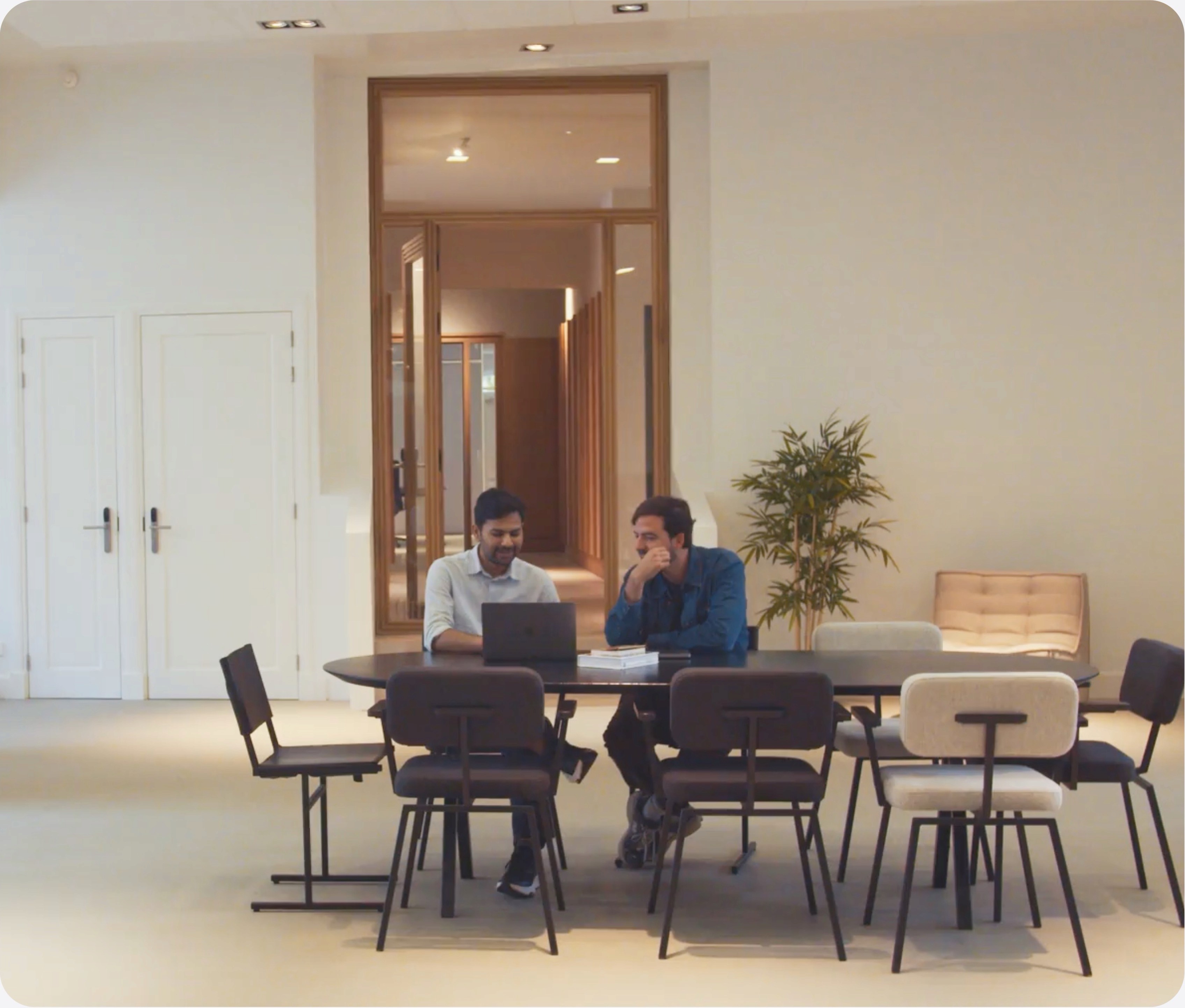 Two people sitting at a table in a bright, modern office space, engaged in a discussion.