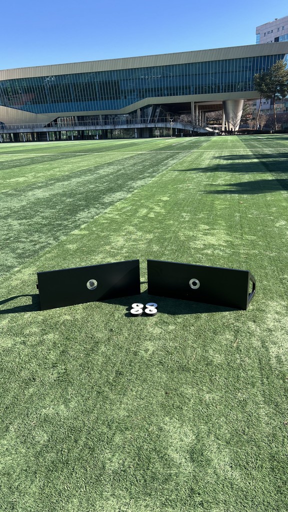 Close-up portrait of a person wearing a gray insulated hooded jacket with the hood up, showing their face framed by the hood against a light background.