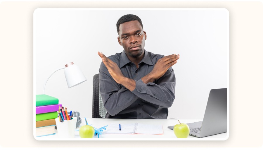 Homme assis au bureau croisant bras, exprimant refus devant ordinateur portable.
