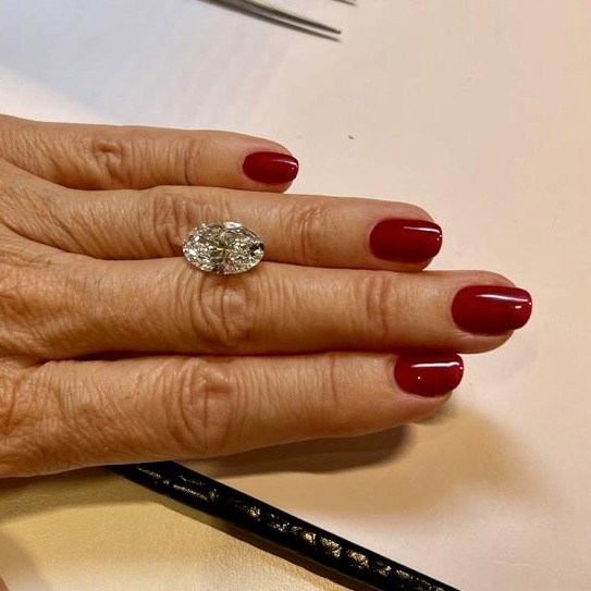 Woman’s hand with red nails showcasing an oval-cut diamond ring, prompting a debate on lab-grown diamonds