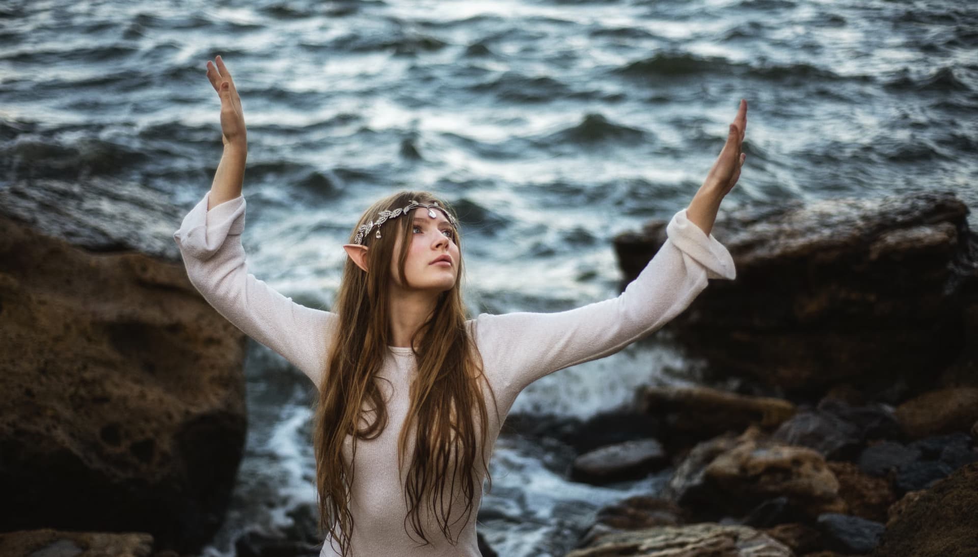 Elf woman in white dress raising hands by the river