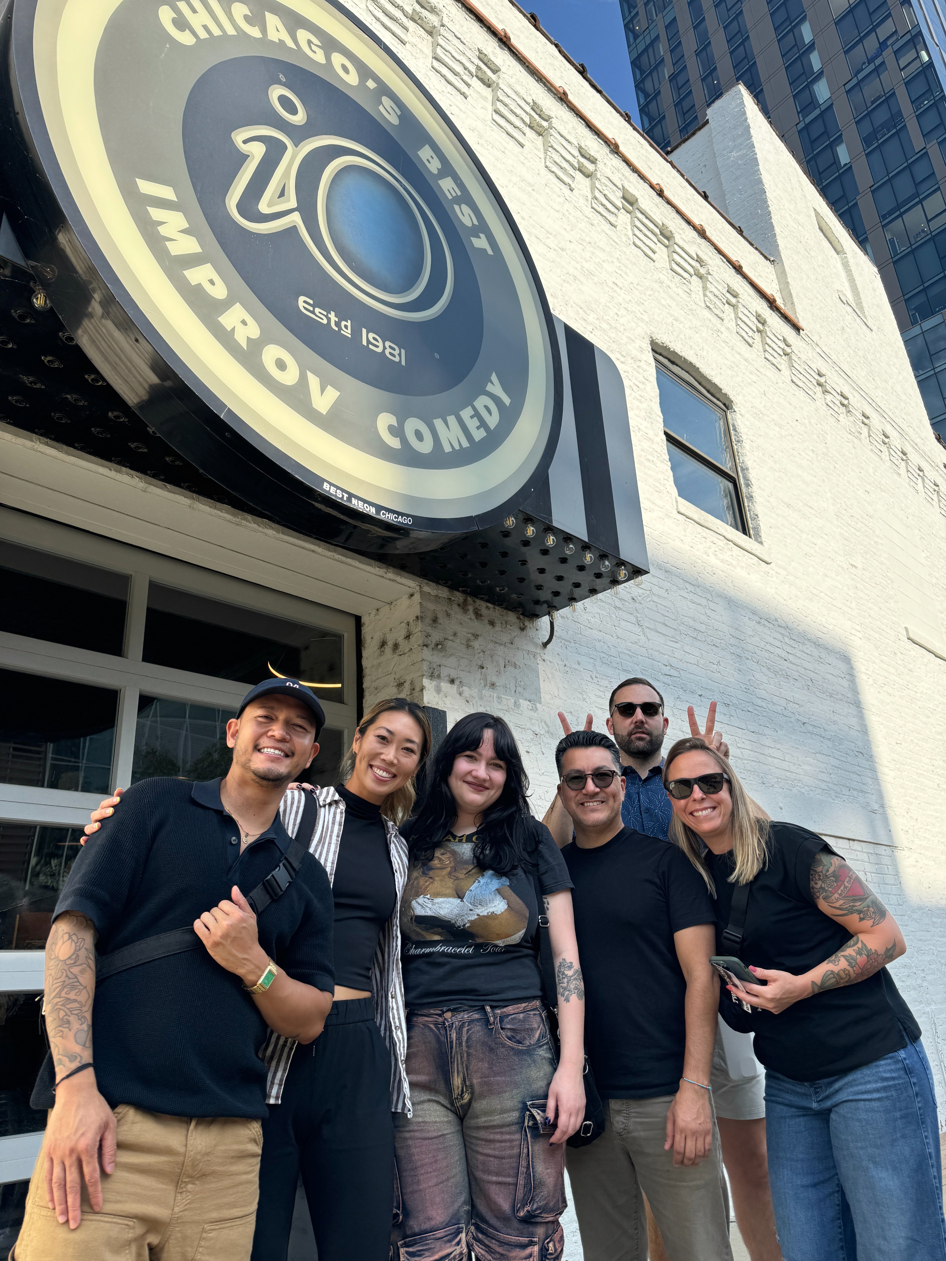 Group of people standing together outside a building with a circular Chicago Improv Comedy sign.