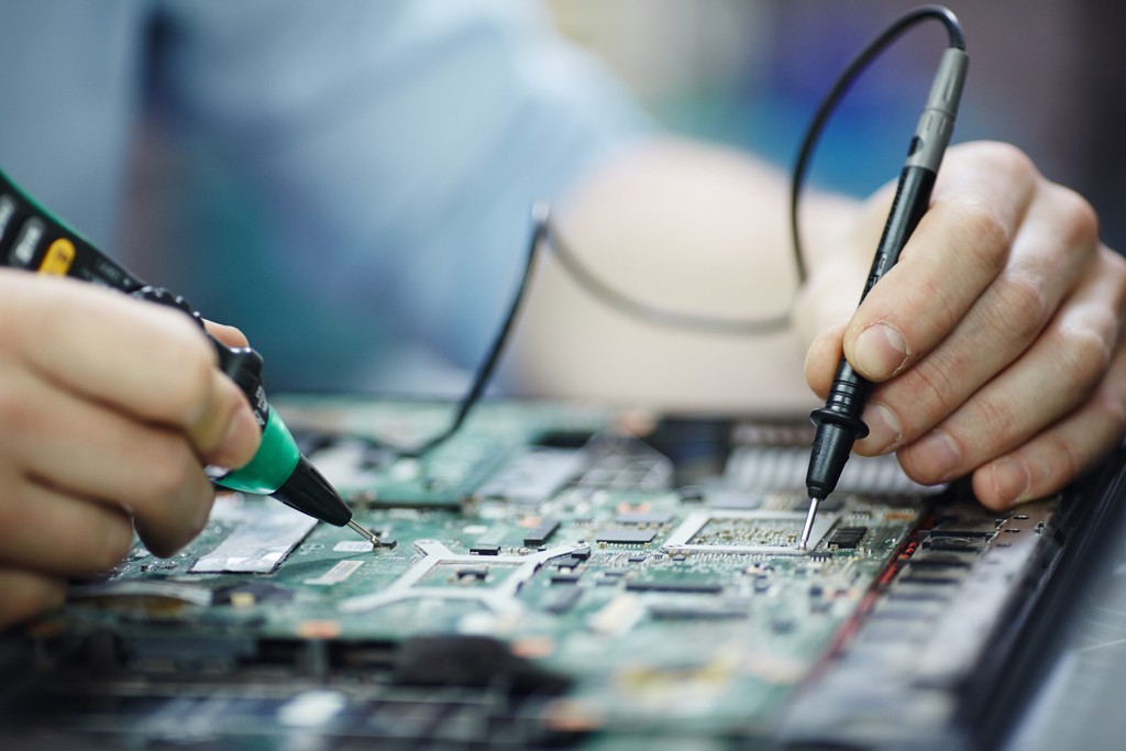 Técnico utilizando multímetro para diagnóstico em placa de circuito impresso, representando manutenção e reparo de hardware e equipamentos eletrônicos em TI - FindUP - Manuteção corretiva