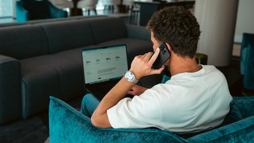 Close-up portrait of a person wearing a gray insulated hooded jacket with the hood up, showing their face framed by the hood against a light background.