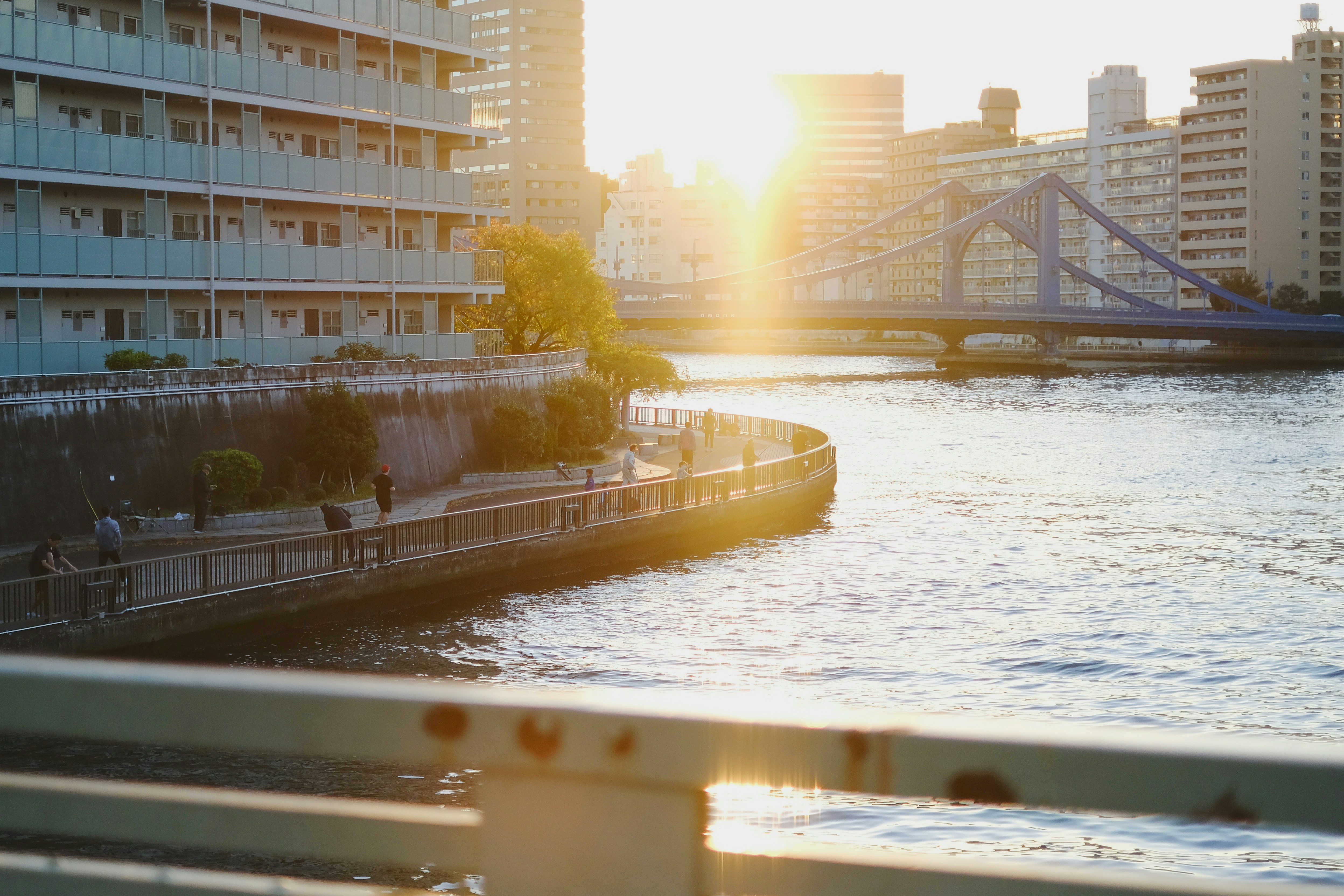 the sun is setting over a river with a bridge in the background