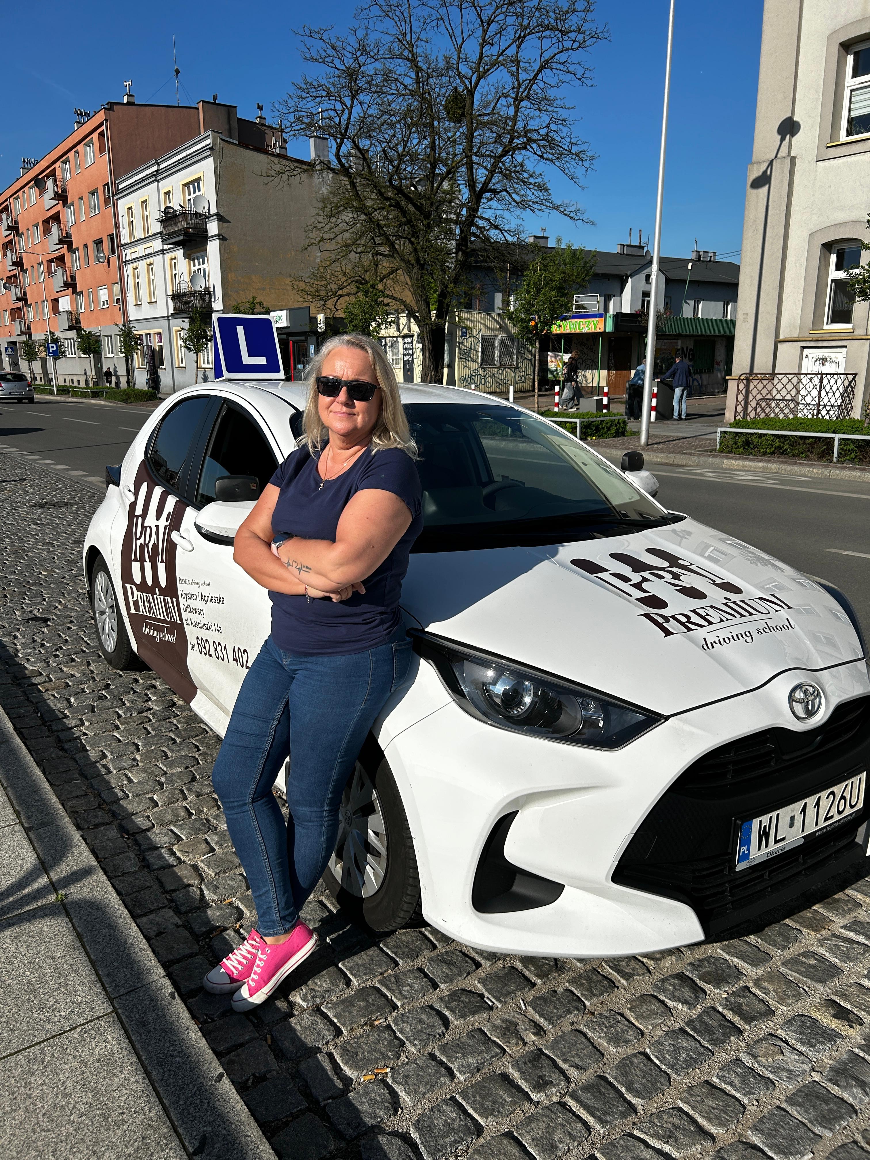 Asia Florczyk-Godzik – Instruktorka pozująca z założonymi rękami przy białej Toyocie Yaris Premium.