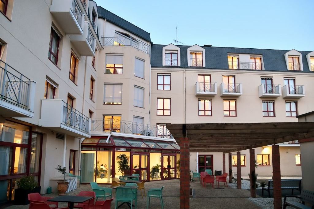 Central courtyard with colorful outdoor furniture, a glass conservatory, and wooden pergola - illuminated windows create a warm, inviting atmosphere