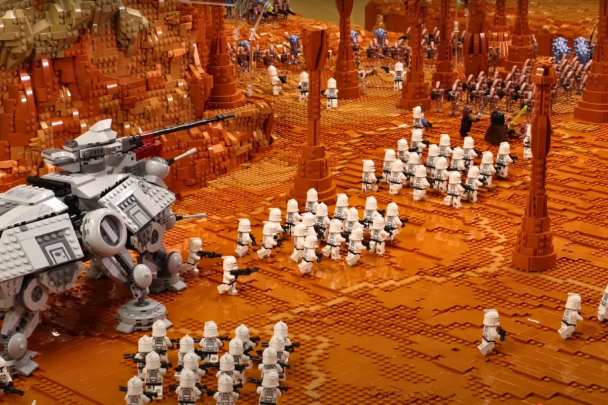 A massive LEGO Star Wars battle scene depicting the Clone Army advancing on the droid forces on Geonosis, featuring an AT-TE Walker, Jedi minifigures, and a large formation of clone troopers engaging in combat.