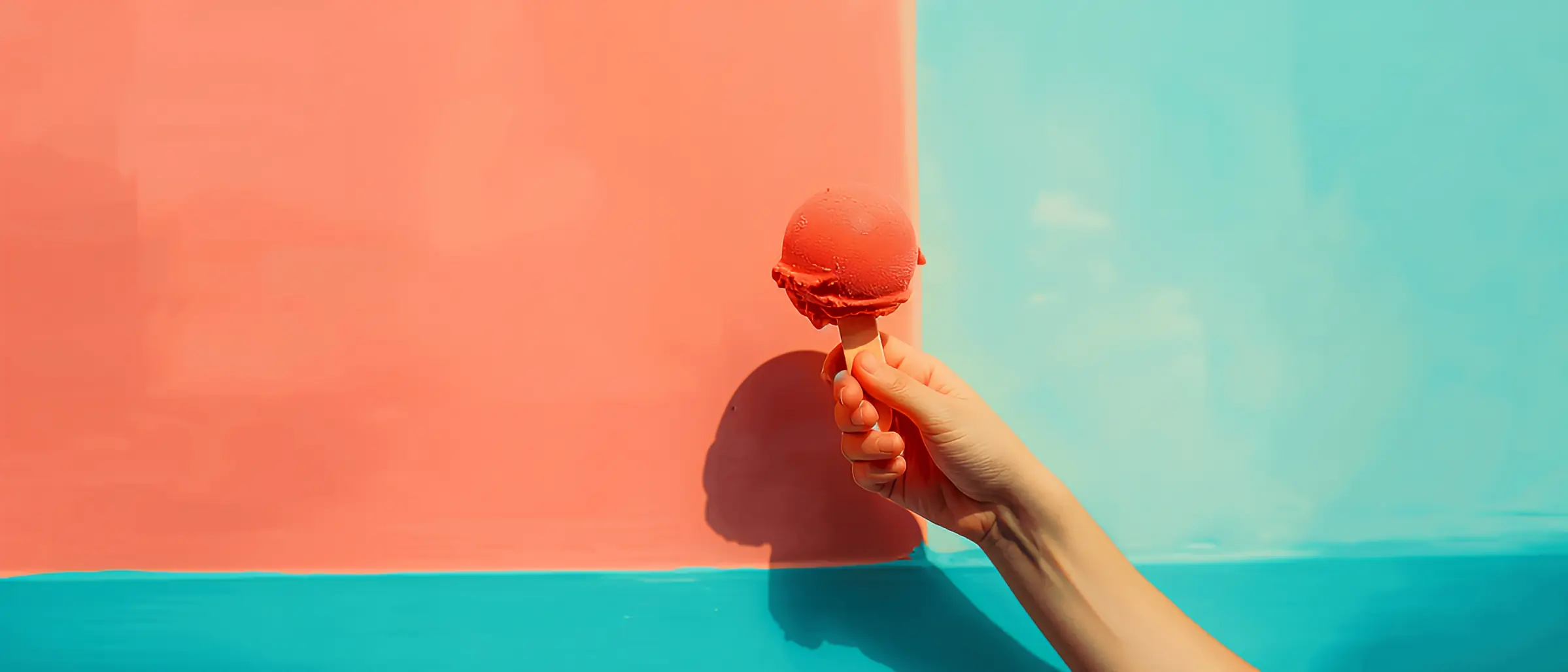 Hand holding ice cream cone in front of a colored wall