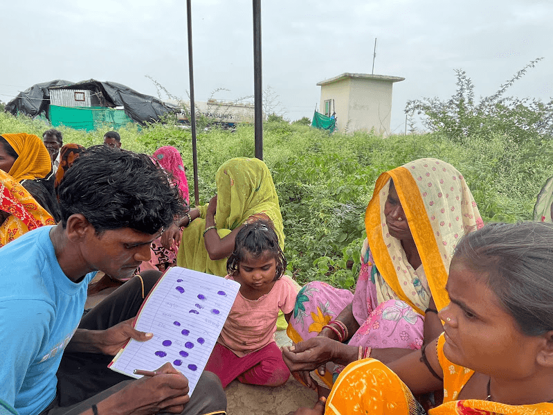 A Sehr team member reviews a forest-rights form with women and children in a village.