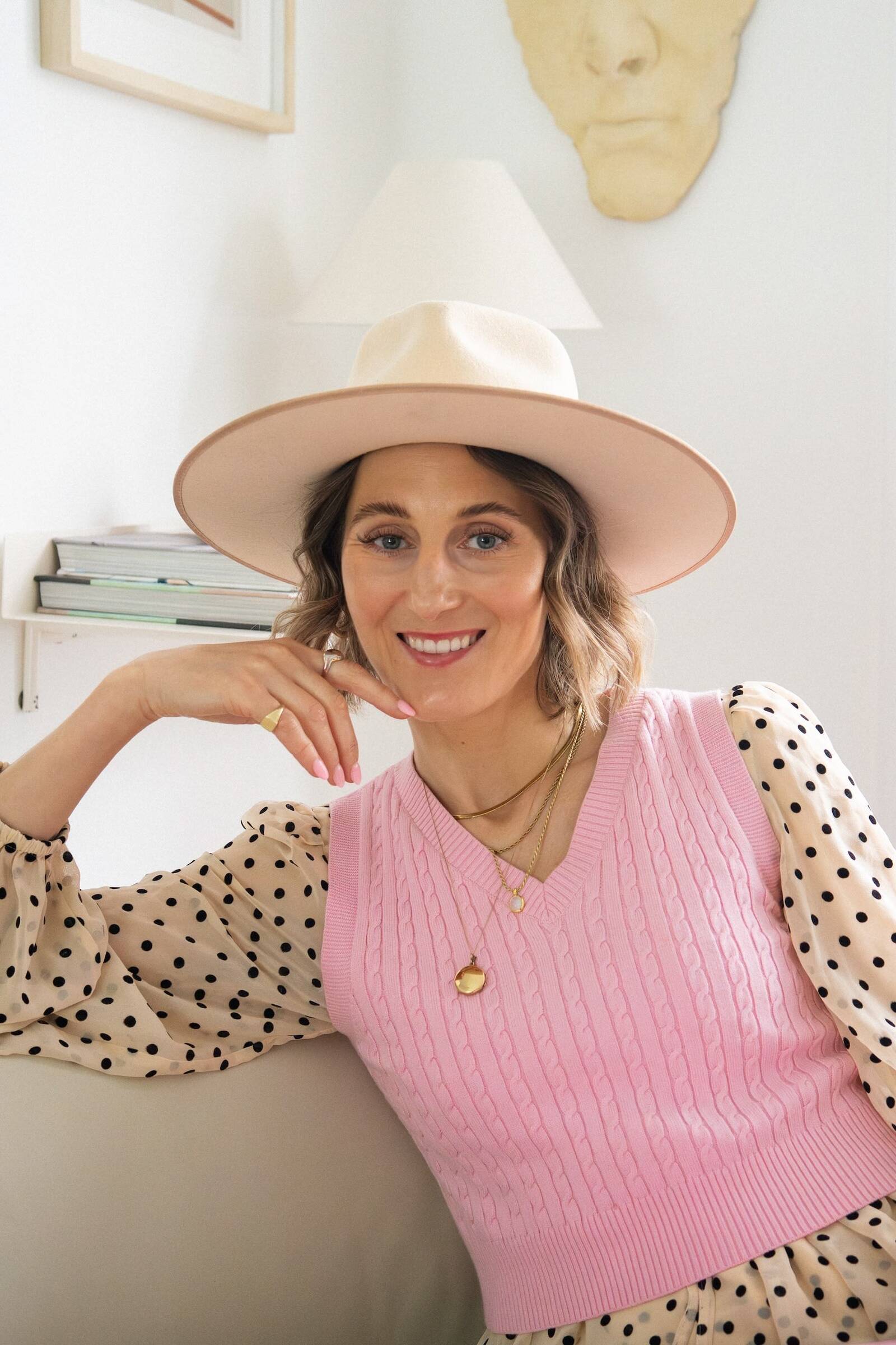 Atelier Akuko founder Judith, wearing a pink sleeveless jumper, polkadot blouse and a wide brimmed hat.