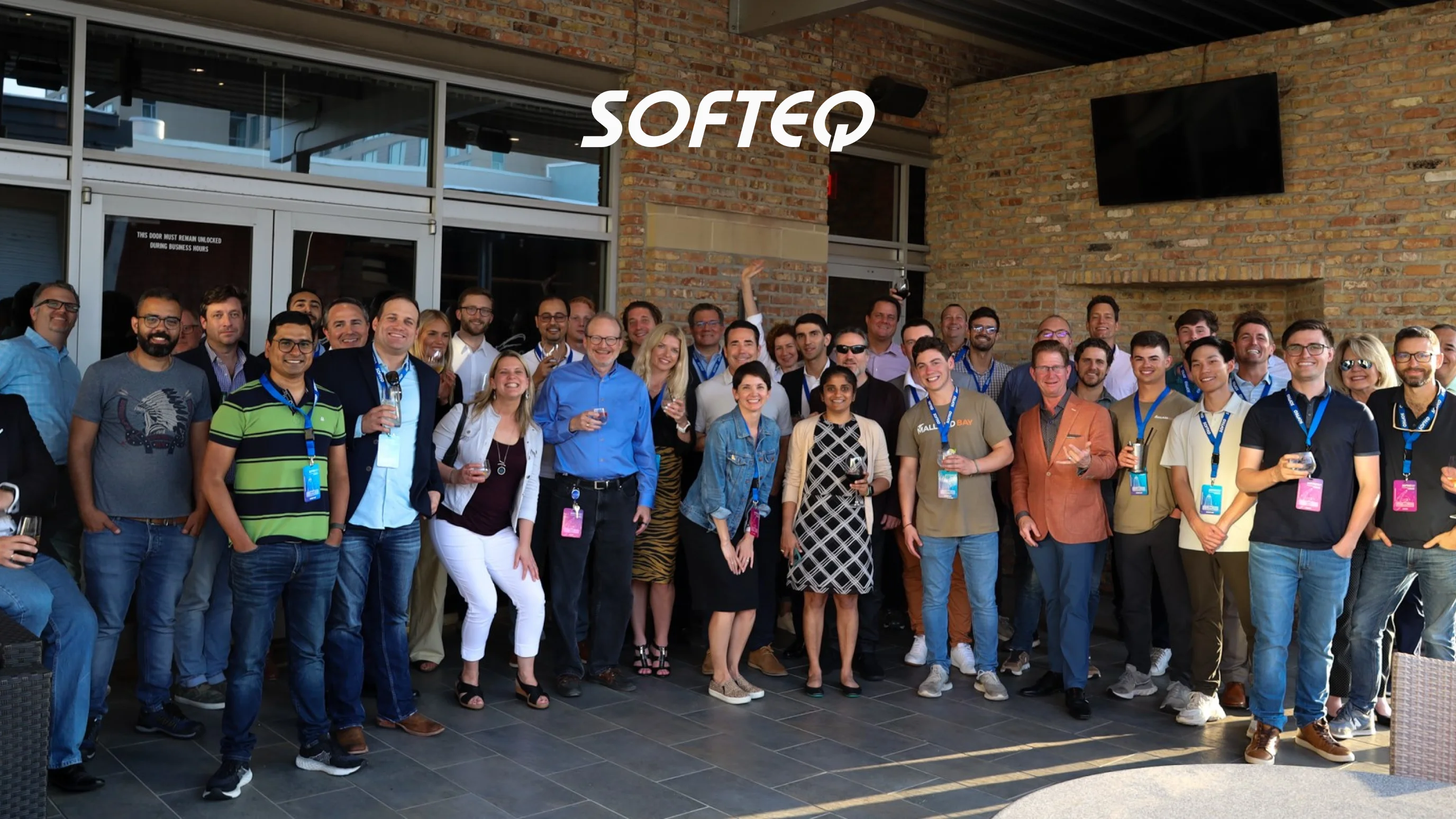 Softeq development company team photo showing a large group of engineers and staff at a casual outdoor event with the Softeq logo displayed above them