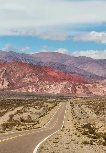 Estrada reta cruzando paisagem árida com montanhas coloridas ao fundo no norte da Argentina