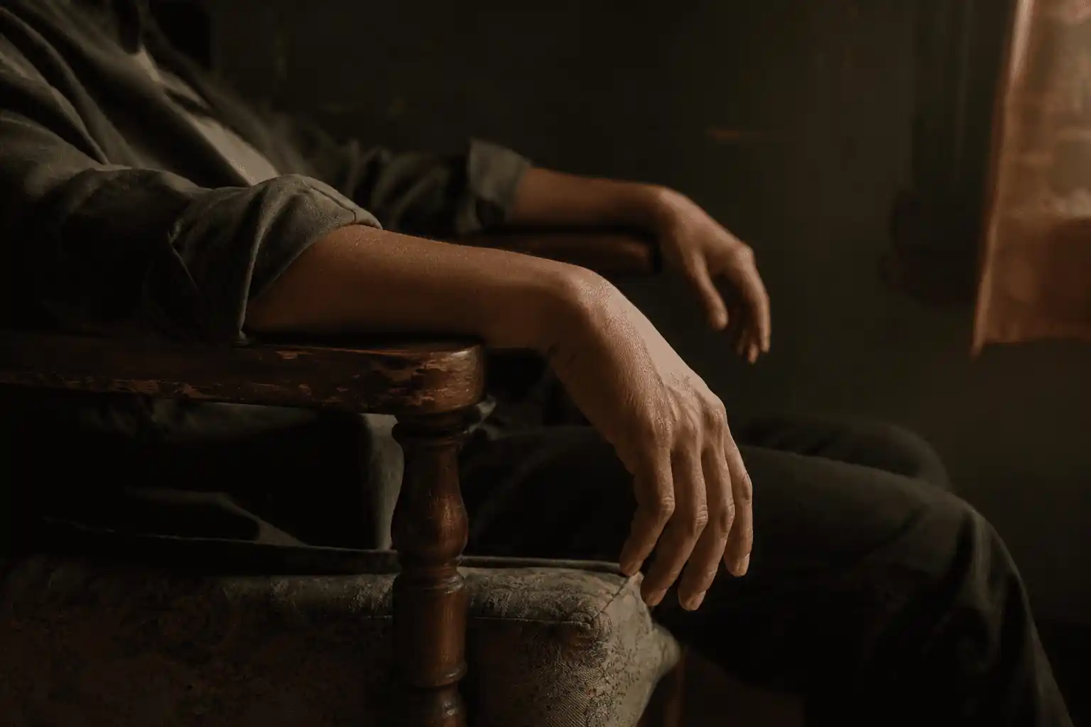 Hands resting quietly on a bed in a dim, reflective room