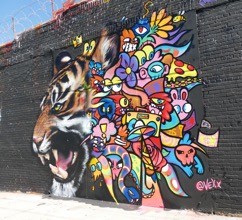 Vibrant street art mural featuring a fierce tiger face on the left transitioning into colorful abstract floral designs in multiple bright colors on a dark wall.