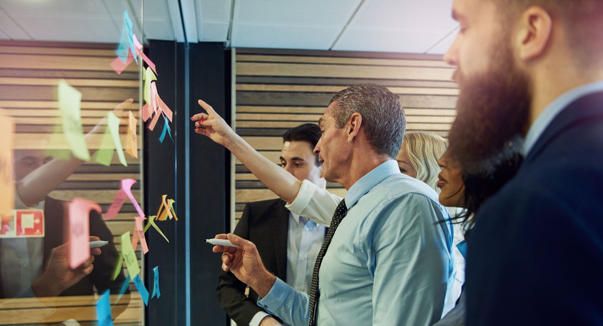 Team members organizing colorful sticky notes on a glass wall during a brainstorming workshop